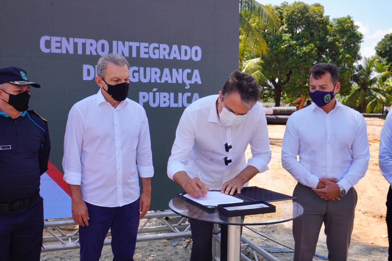 Camilo Santana assinando documento disposto em mesa, Sarto ao lado esquerdo e senhor ao lado direito, ambos em pé
